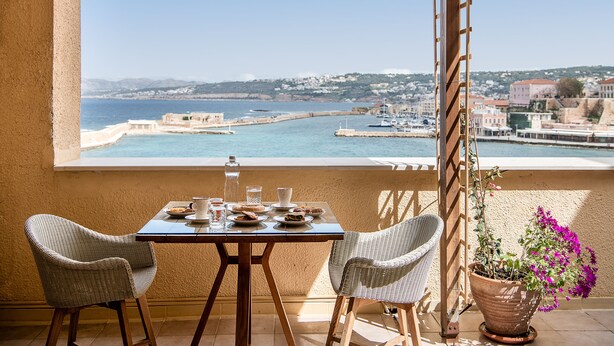 A balcony with a table set for two, overlooking a coastal town and harbor. - San Salvatore Monastery (Chania)