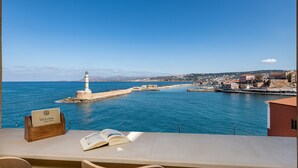 A view from a balcony overlooking a coastal town with a lighthouse, a clear blue sky, and a welcoming sign. - San Salvatore Monastery (Chania)