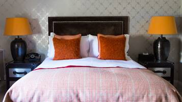 A neatly made bed with a checkered bedspread and two pillows, flanked by two nightstands with lamps and a vintage telephone.