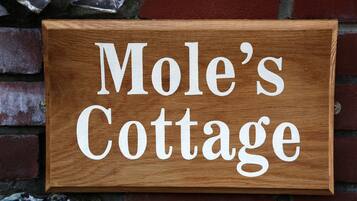 A wooden sign with the text "Mole's Cottage" mounted on a brick wall.
