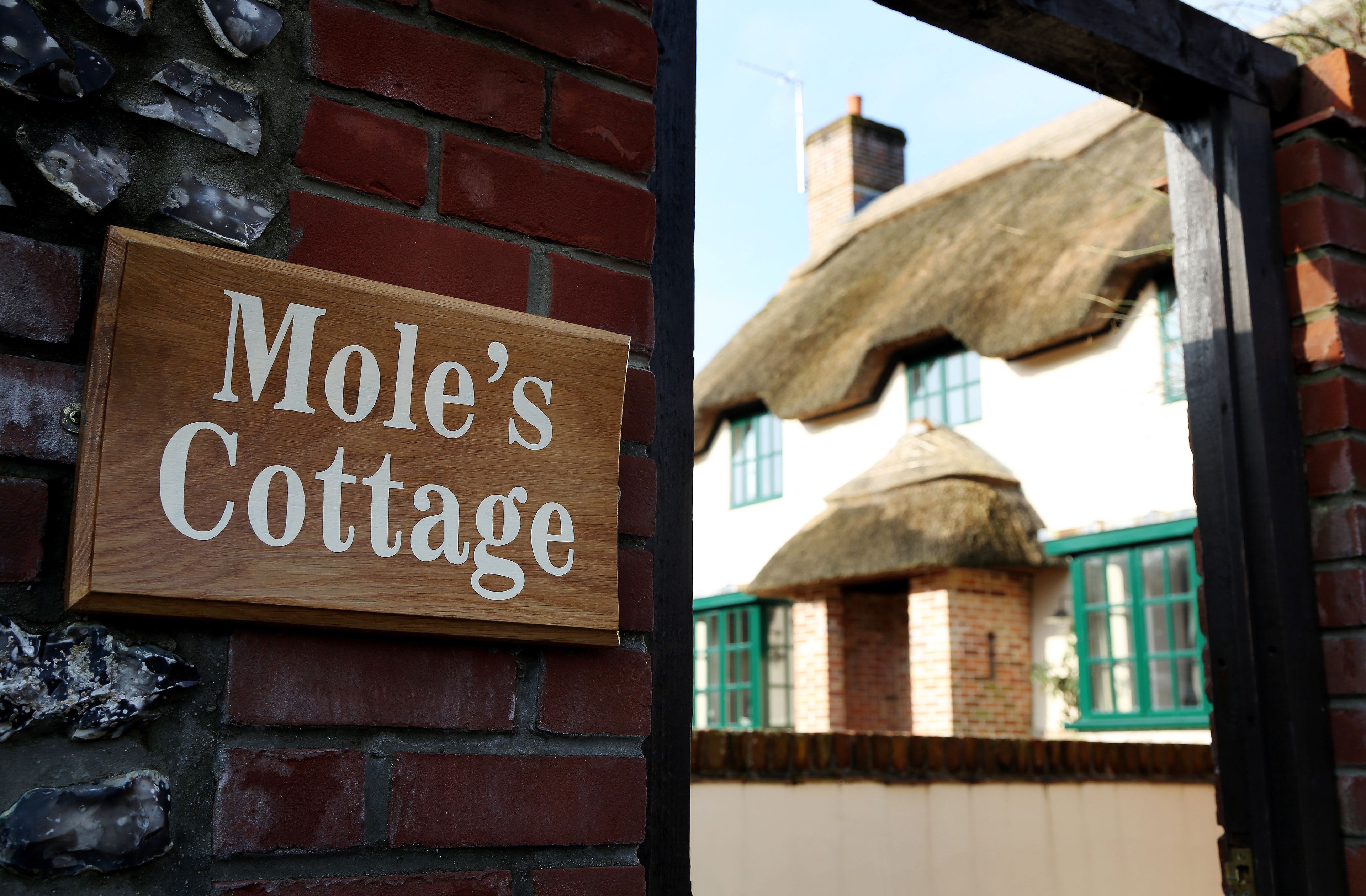 Un letrero de madera con el texto "Mole's Cottage" sujeto a una pared de ladrillo.