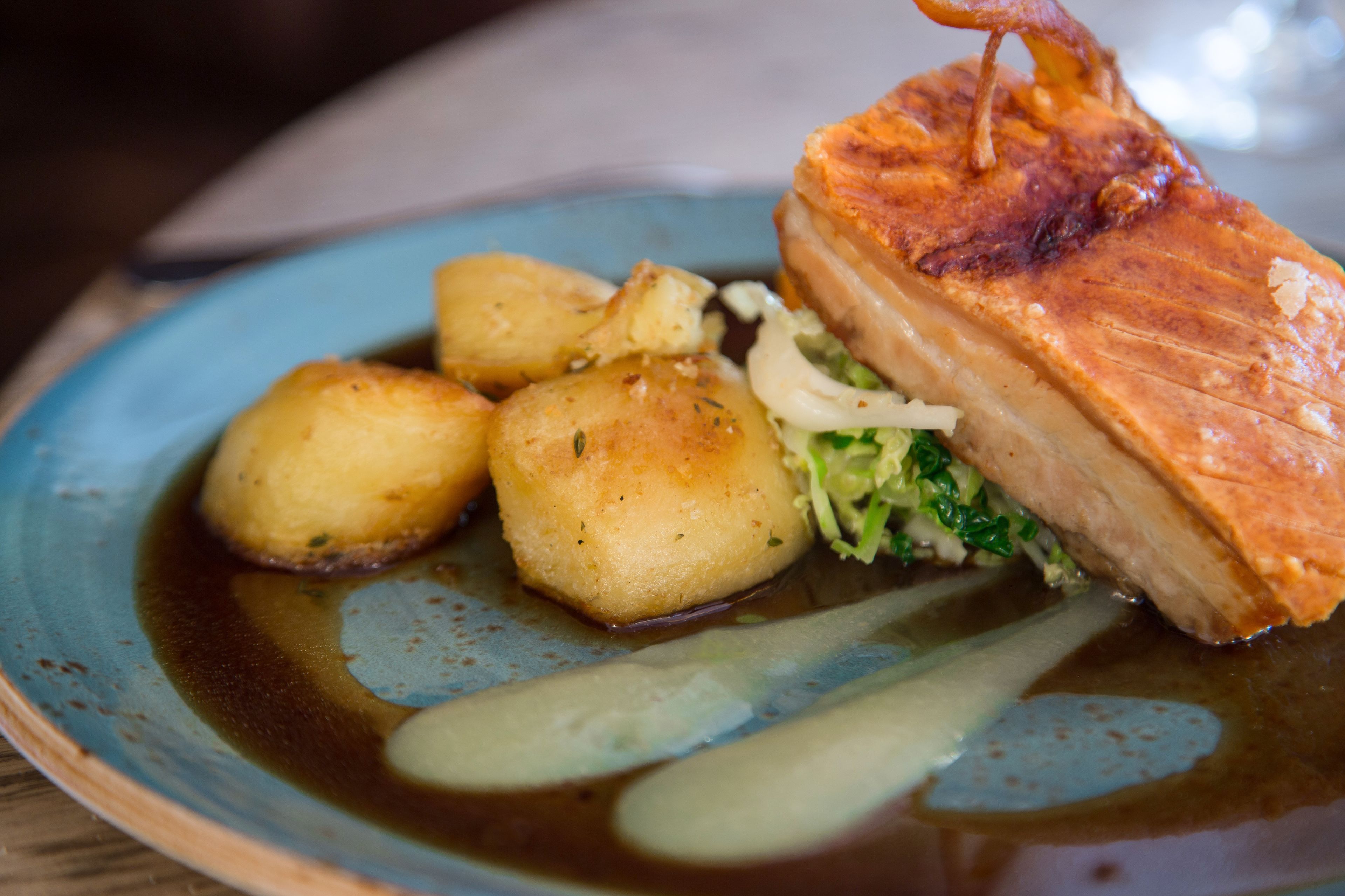 Ein Teller mit gebratenem Schweinshaxn, Salzkartoffeln und einem Beilagengrün.