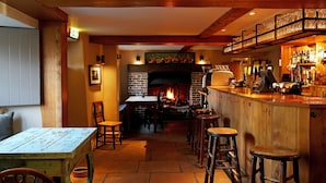 A cozy bar area with a fireplace, wooden bar counter, stools, and a table with a menu. - The Museum Inn (Blandford Forum)