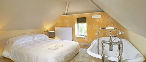 A bedroom with a single bed, a window, a radiator, and a bathroom with a bathtub and shower.