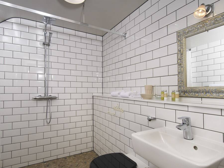 Ein Badezimmer mit weißen, rechteckigen Fliesen, einer Dusche, einem Waschbecken und einem Spiegel mit aufwendiger Rahmung.