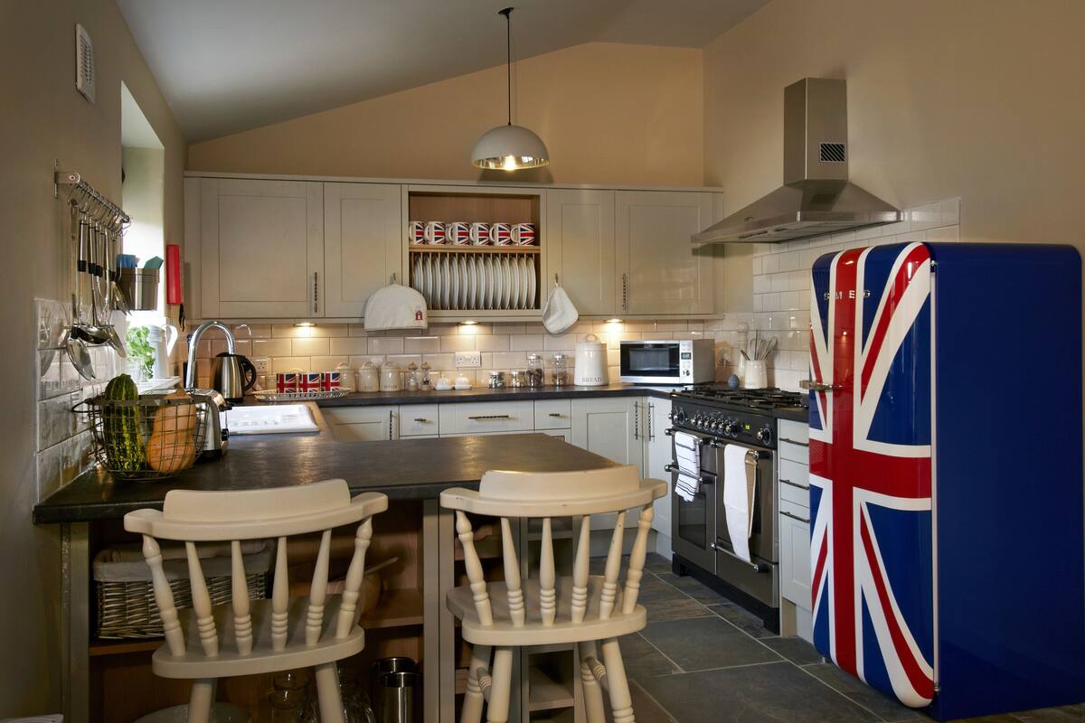 A kitchen with white cabinets, a blue refrigerator with a Union Jack design, a gas stove, and a hanging light fixture.