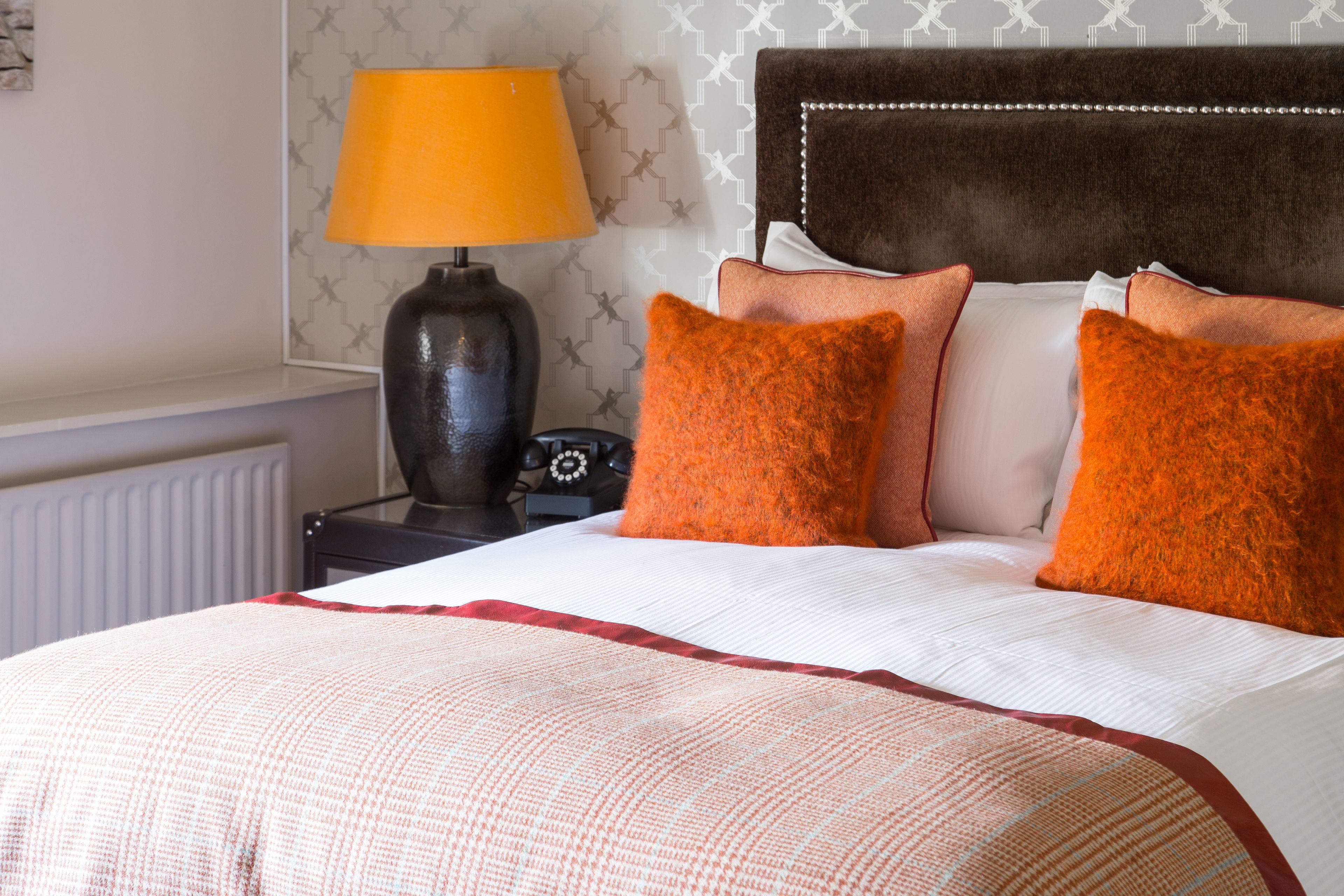 A neatly made bed with a white and red striped blanket, two orange pillows, and a brown headboard.