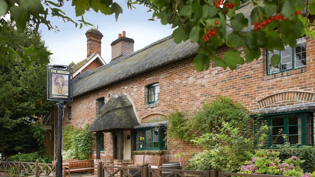 A traditional brick building with a thatched roof, a signboard, and a wooden fence. - The Museum Inn (Blandford Forum)