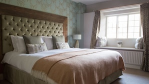 A bedroom with a large bed, a wooden headboard, a window with curtains, and a radiator. - The Museum Inn (Blandford Forum)