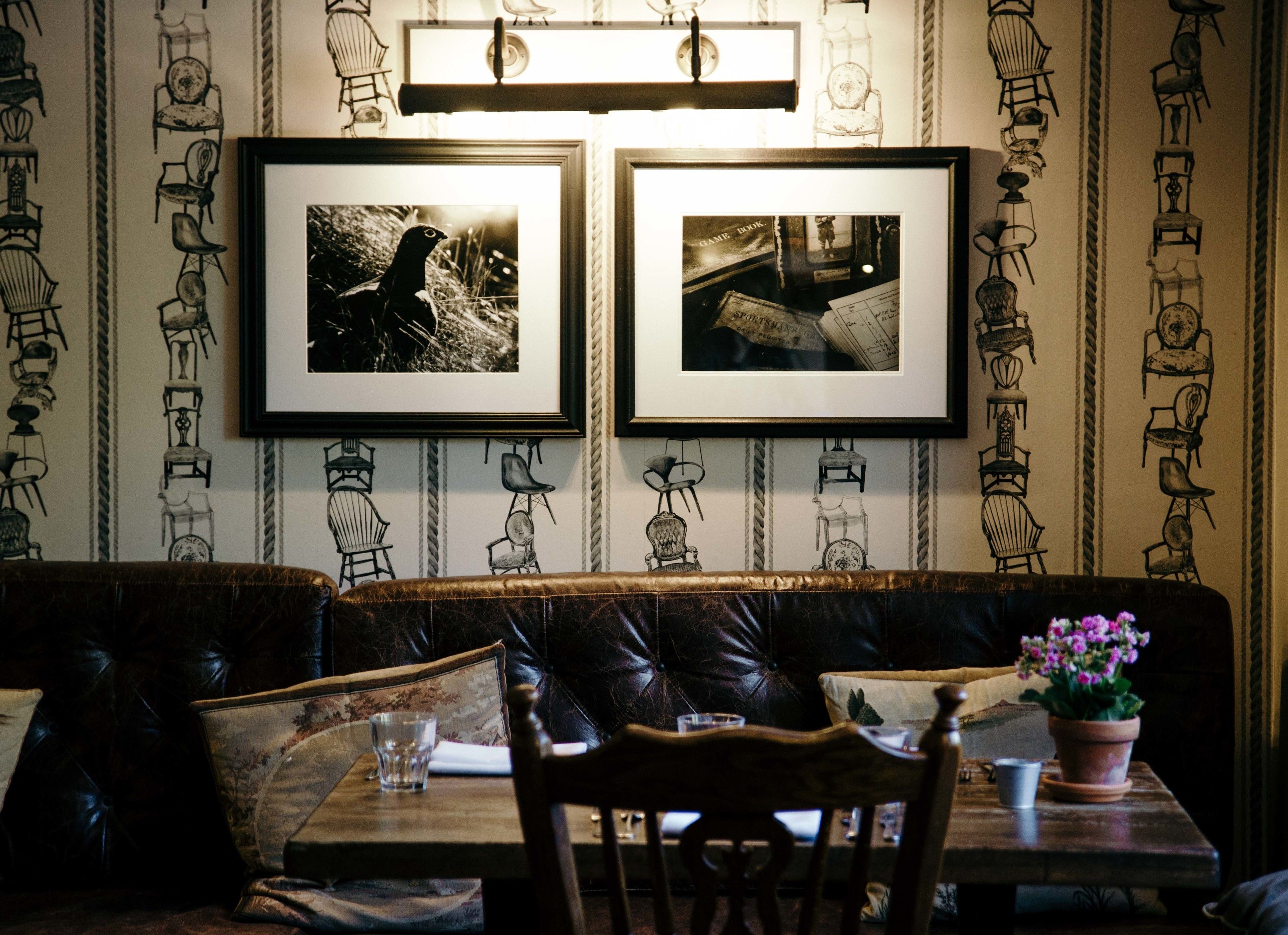 A restaurant interior with a leather booth seating area, framed pictures on the wall, and a table with a potted plant.