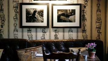 A restaurant interior with a leather booth seating area, framed pictures on the wall, and a table with a potted plant.