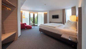 A modern hotel room with a large bed, a desk, a chair, and a TV. - Hotel Susato (Soest)