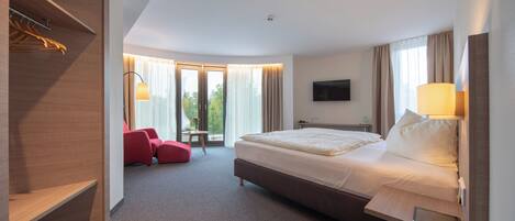 A modern hotel room with a large bed, a desk, a chair, and a TV.