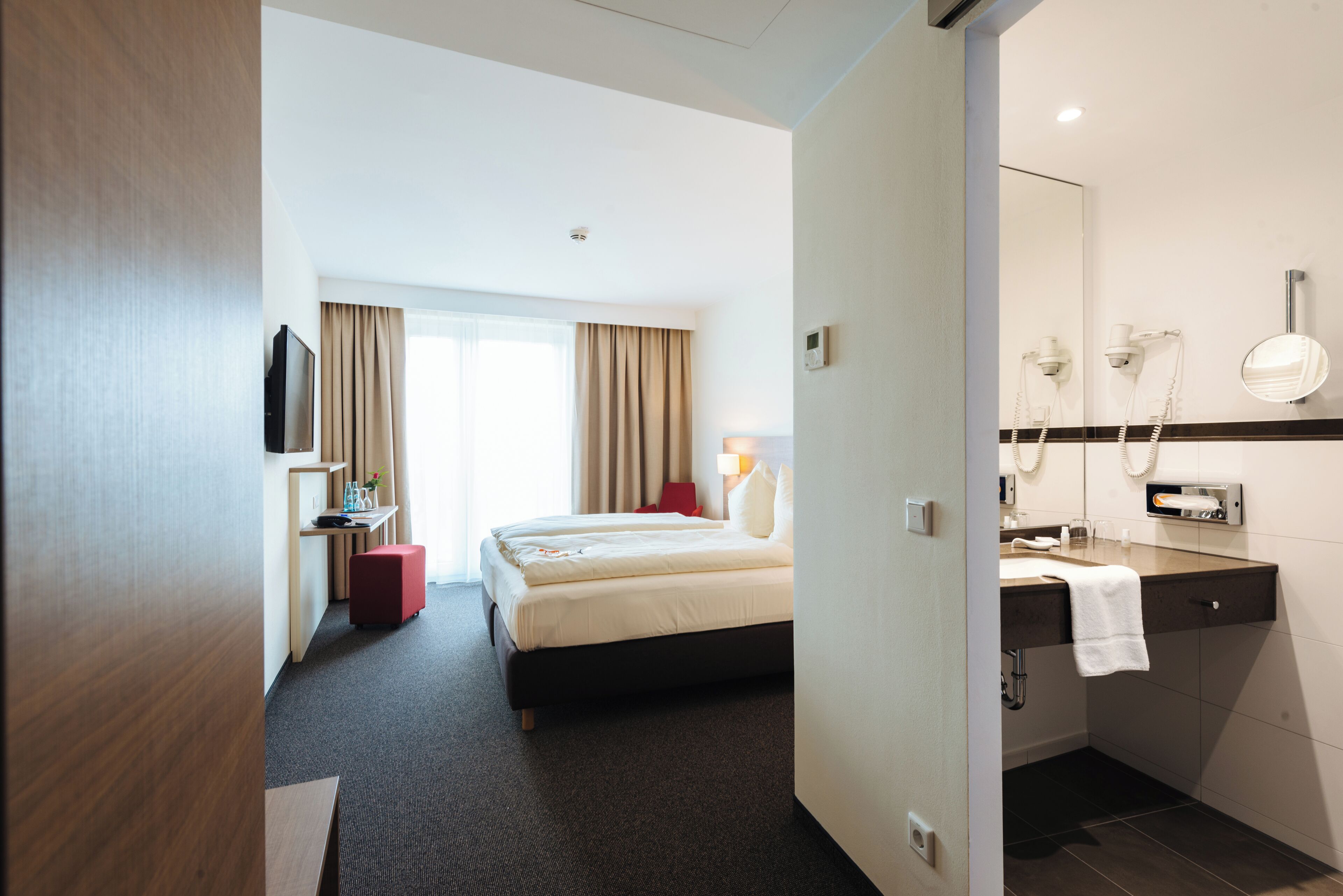 Hotelkamer met een bed, een bureau met een computer, een televisie en een badkamer met spiegel en handdoekhouder.