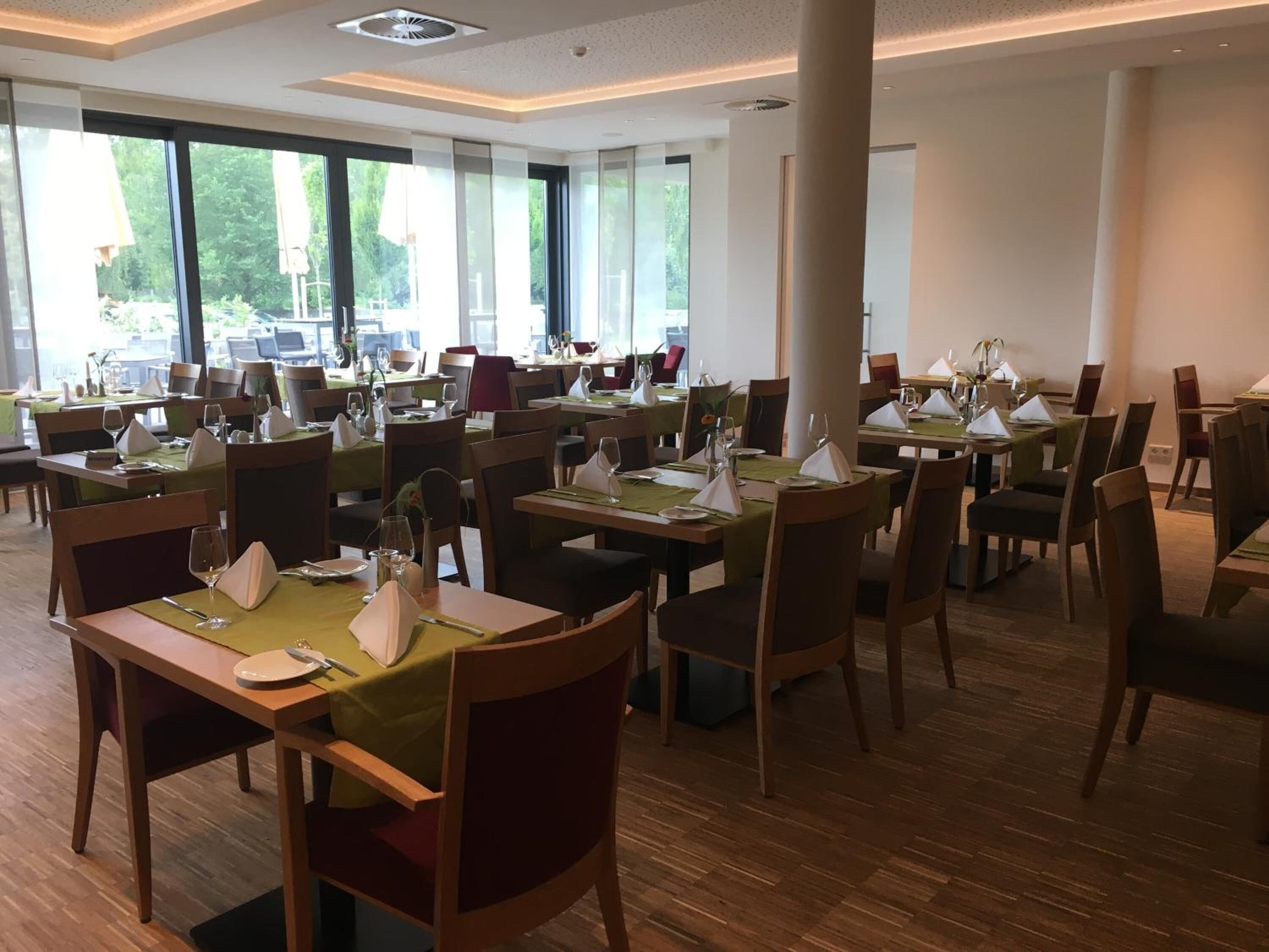 A spacious dining area with multiple tables and chairs, large windows offering a view of the outdoors, and a clean, modern interior design.