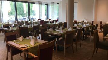 A spacious dining area with multiple tables and chairs, large windows offering a view of the outdoors, and a clean, modern interior design.