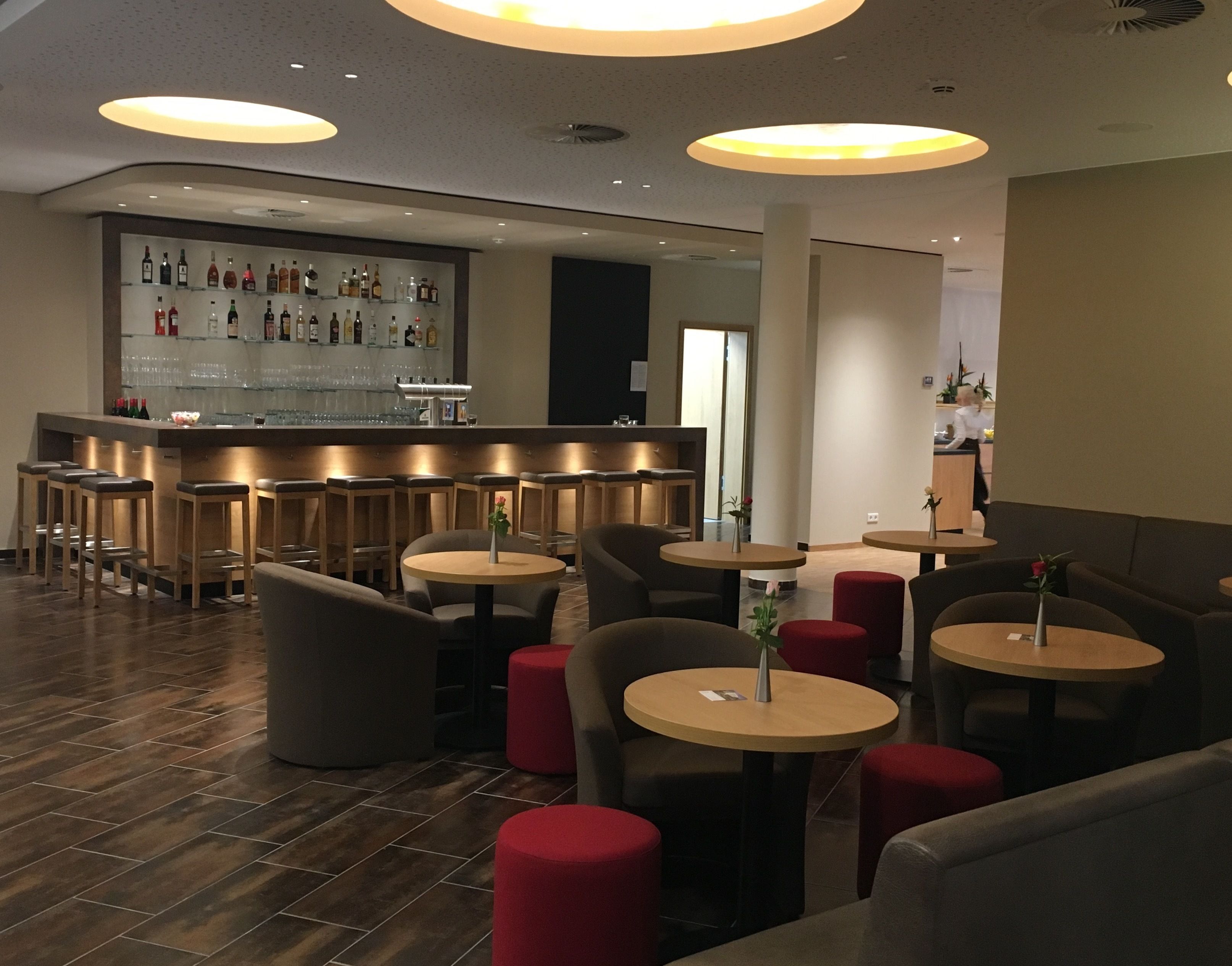 Eine moderne Bar mit einer Auswahl an Spirituosenflaschen und Gläsern auf Regalen, umgeben von Sitzgelegenheiten mit runden Tischen und gepolsterten Stühlen.