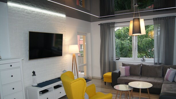 A modern living room with a flat-screen TV, yellow armchair, sofa, and a small round table. - Apartamenty Usteckie - Na Wydmie (Ustka)