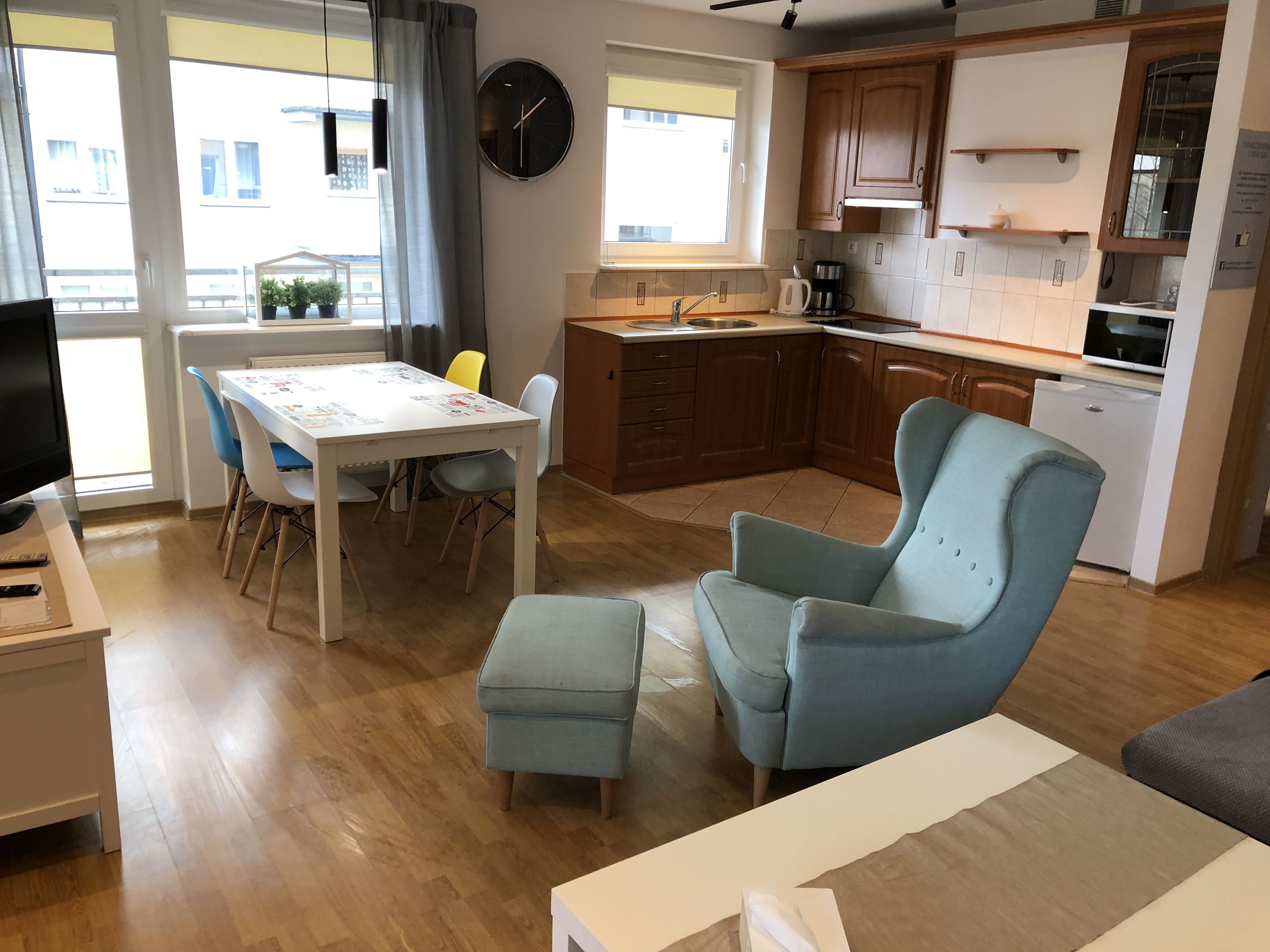 A modern living room with a dining table, two chairs, a blue armchair, and a television on a stand.