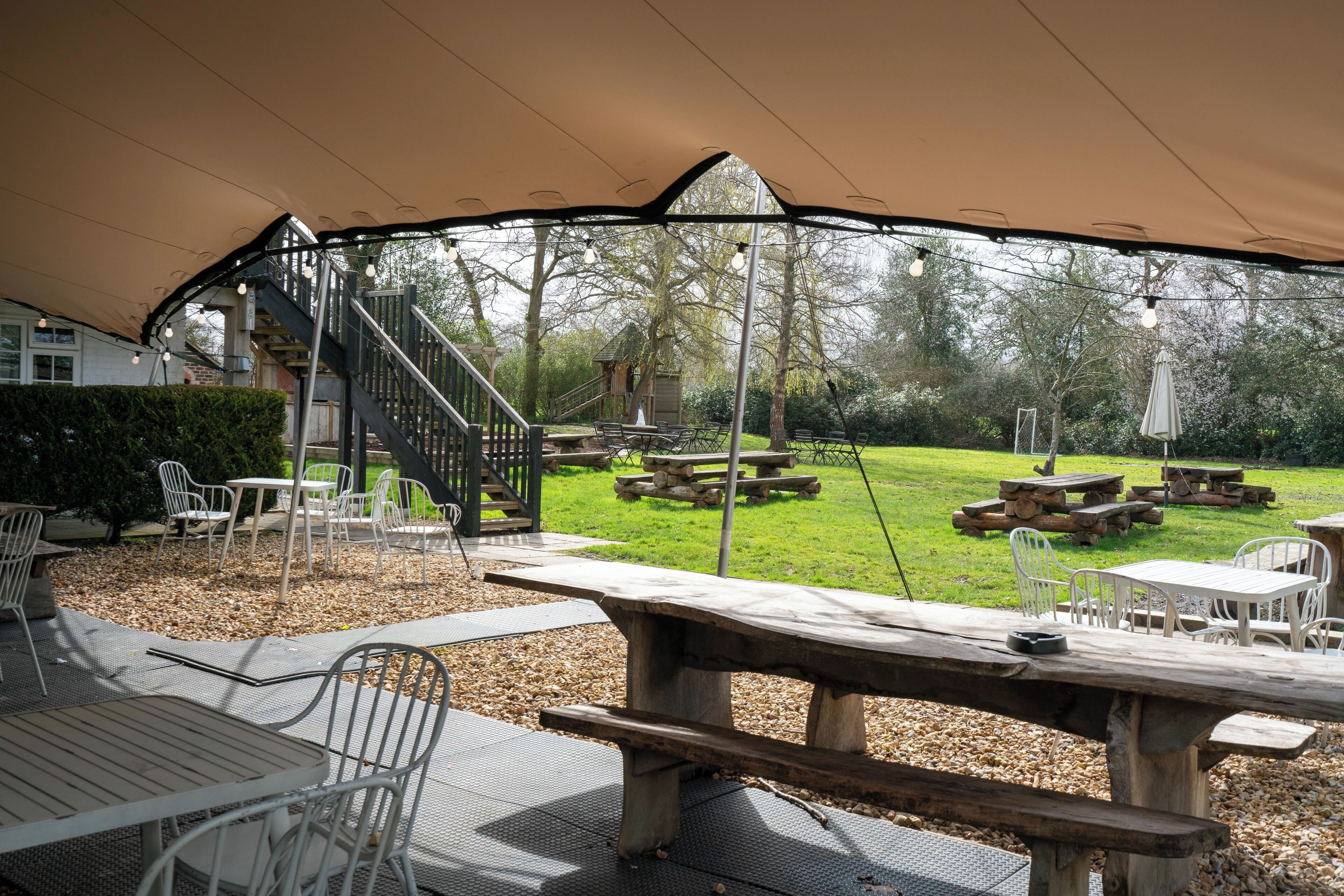 An outdoor patio area with picnic tables and chairs, a covered seating area, and a staircase leading to a deck.