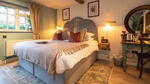 A bedroom with a large bed, a wooden headboard, a bedside table with a lamp, a mirror, and a view of the outdoors through a window. - The Old House Inn (Crawley)