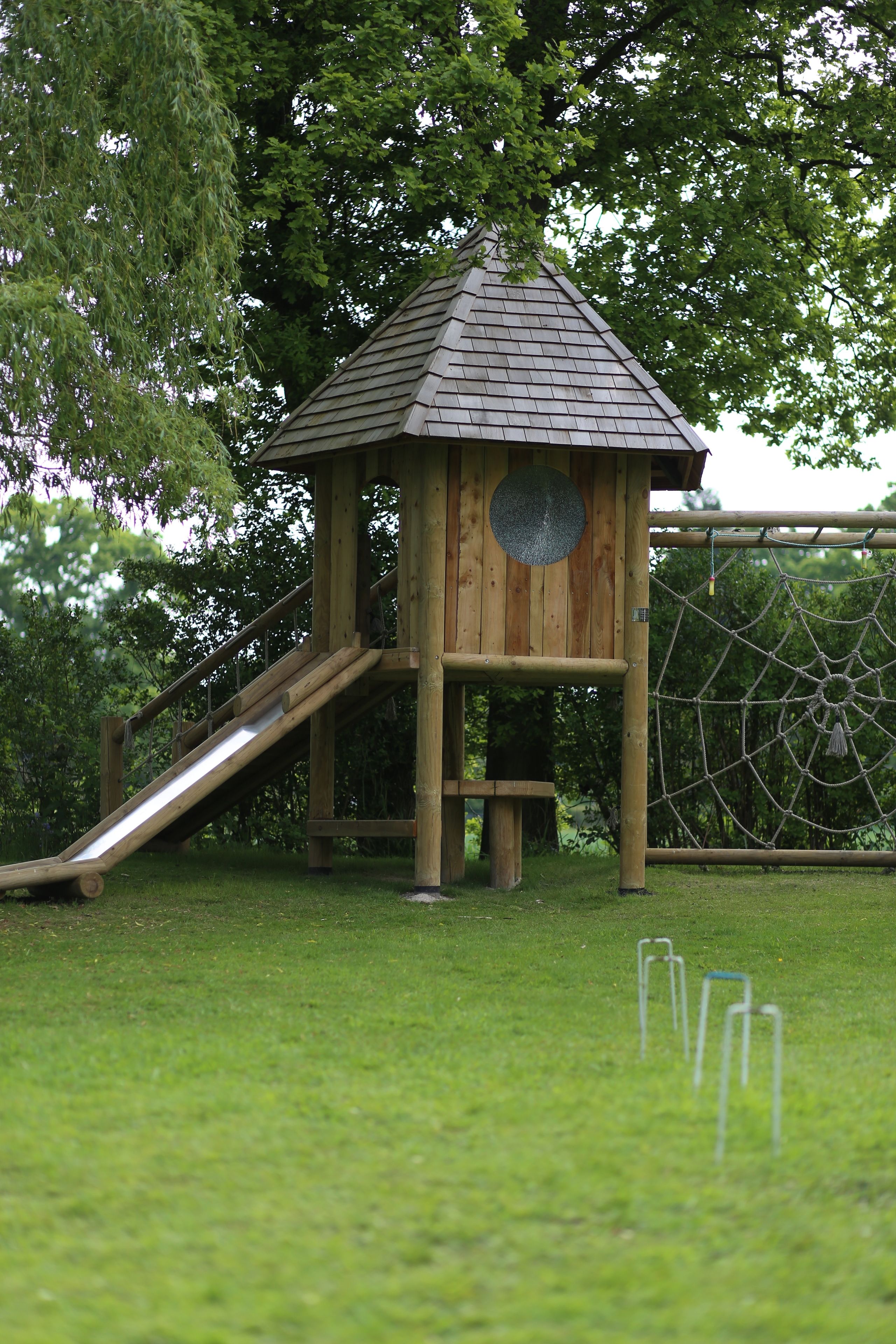 Une structure de jeu en bois, dotée d’un toboggan et d’un filet en corde.