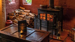 A rustic room with a traditional wood-burning stove, a table with a candle, and a window with a view of greenery. - The Old House Inn (Crawley)