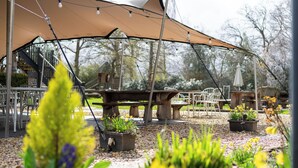 An outdoor seating area with tables and chairs under a canopy, surrounded by potted plants and flowers. - The Old House Inn (Crawley)