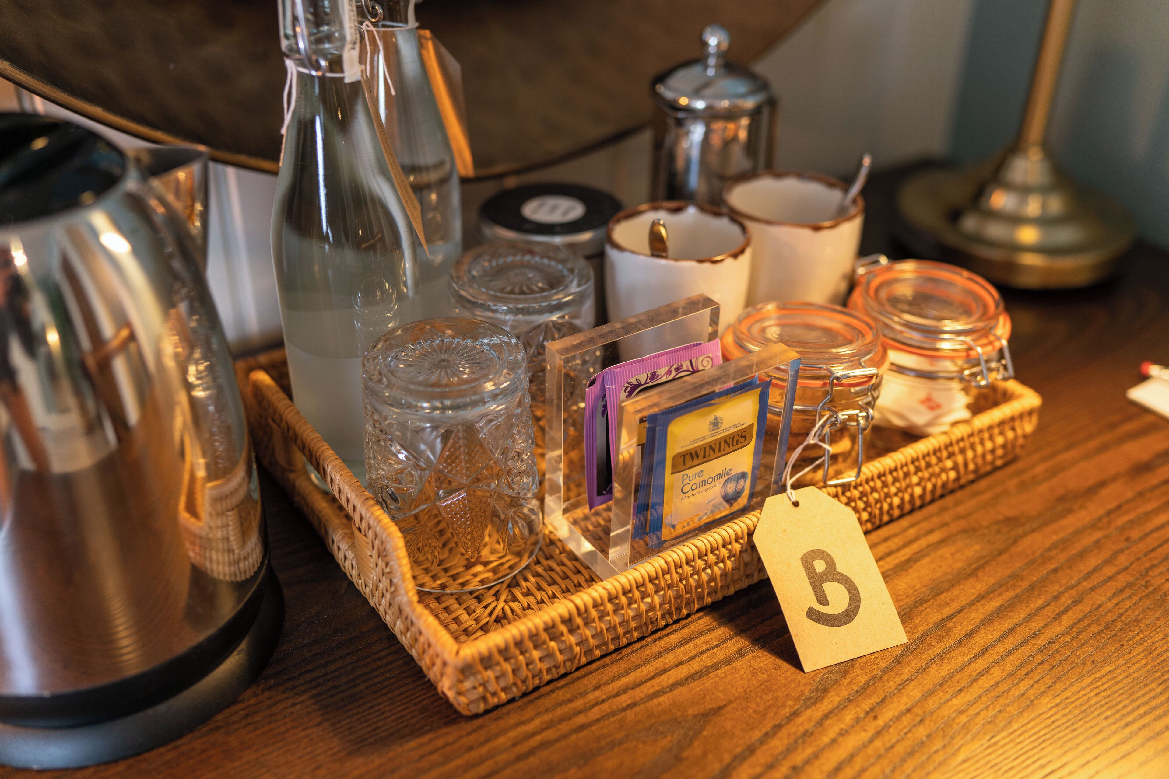 A wooden table with a tray holding various items including a kettle, glass jars, a candle, and a box of Twinings tea.