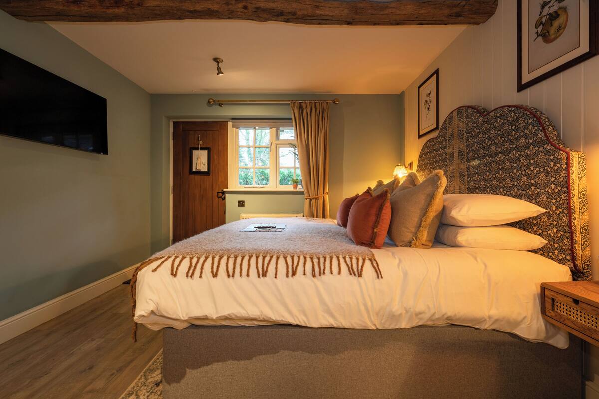 A bedroom with a large bed, a wooden headboard, a bedside table, and a window with curtains.