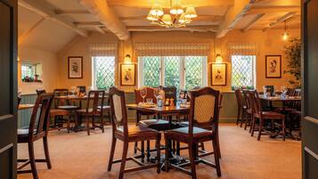A dining area with wooden tables and chairs, a chandelier, and windows with patterned curtains.
