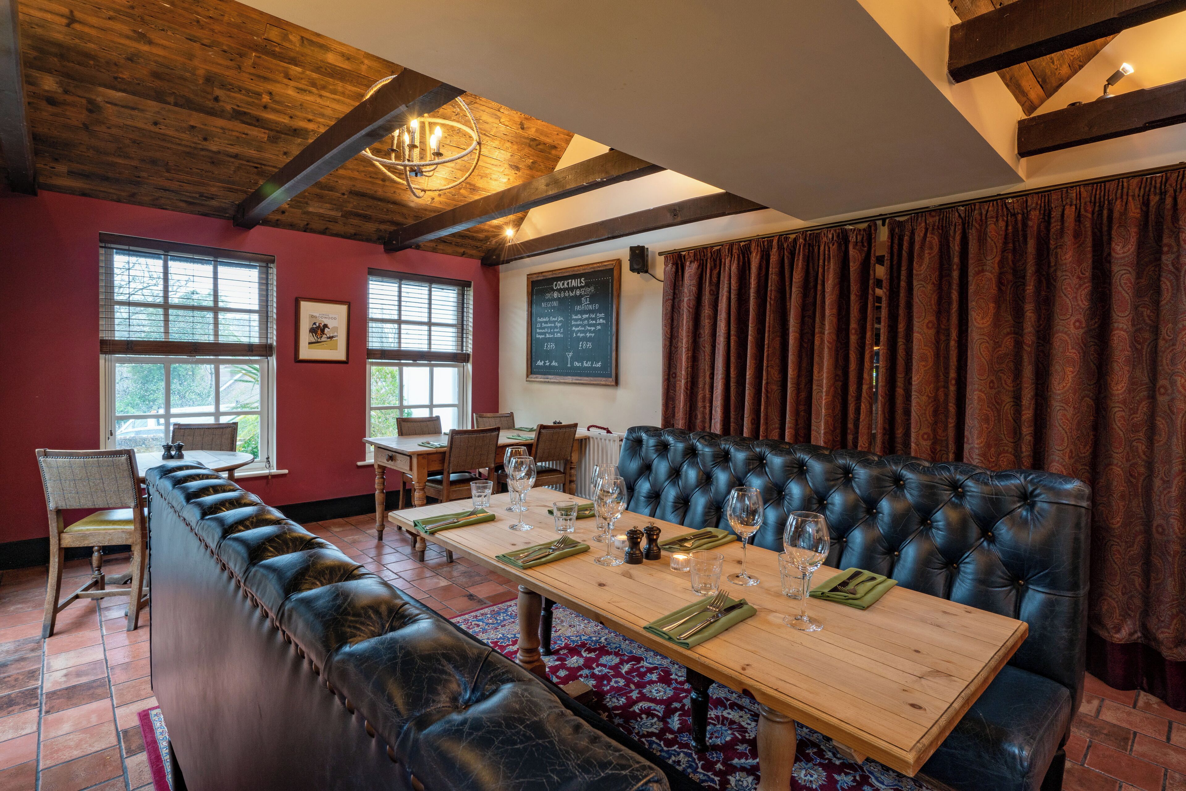 A dining area with a long wooden table set for a meal, a black leather bench, and a chandelier.
