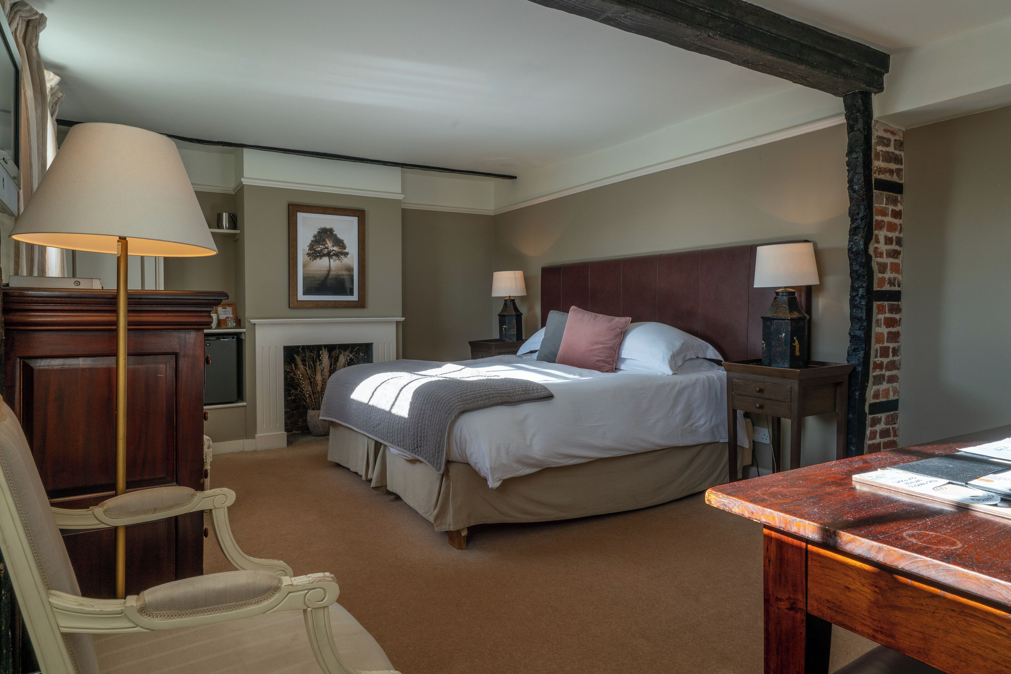 A bedroom with a large bed, two bedside tables with lamps, a wooden chair, a desk, and a fireplace.