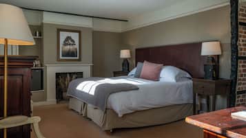 A bedroom with a large bed, two bedside tables with lamps, a chair, a fireplace, and a framed picture on the wall.