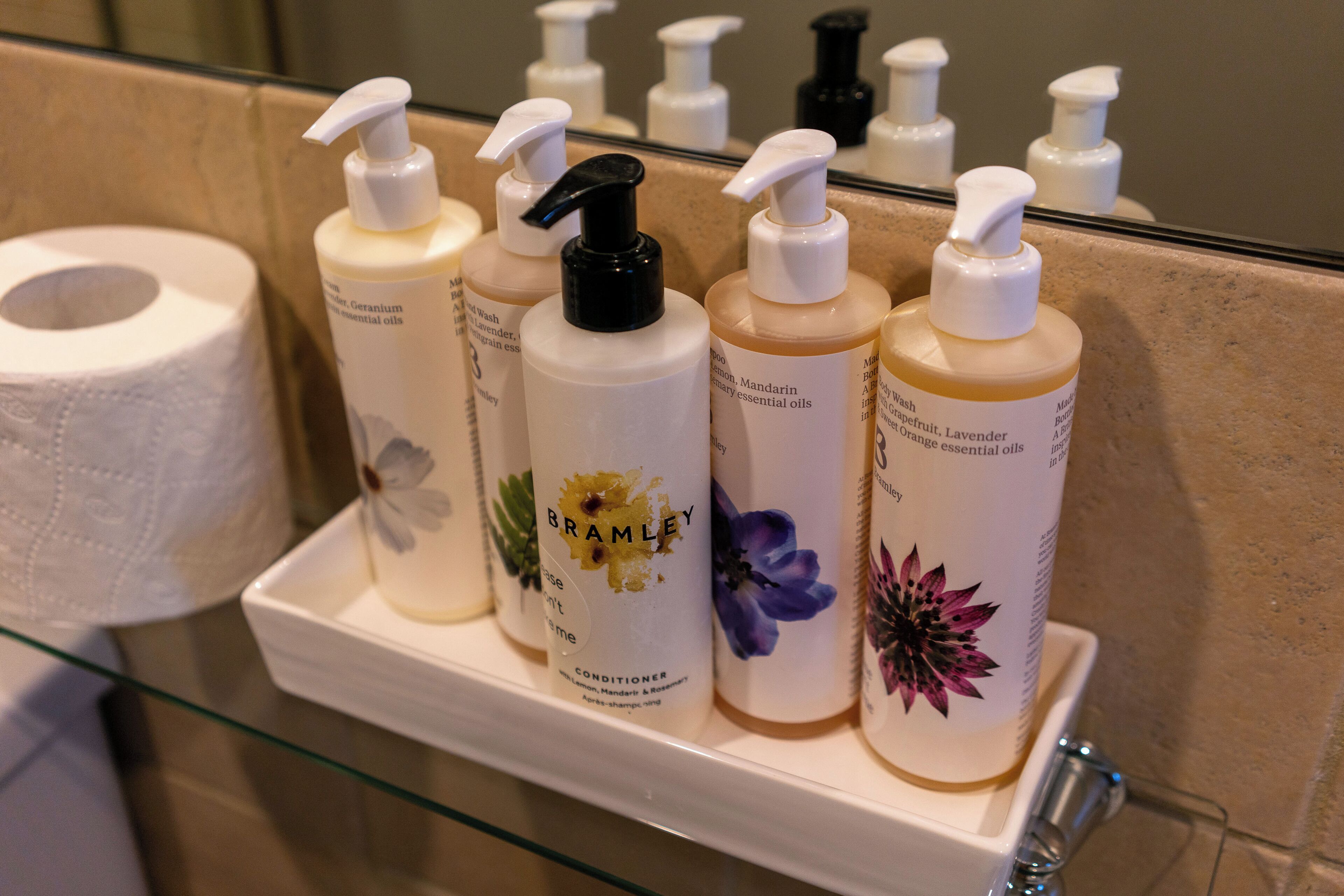 A bathroom shelf with various toiletries including a toilet paper roll, bottles of essential oils, and a conditioner.
