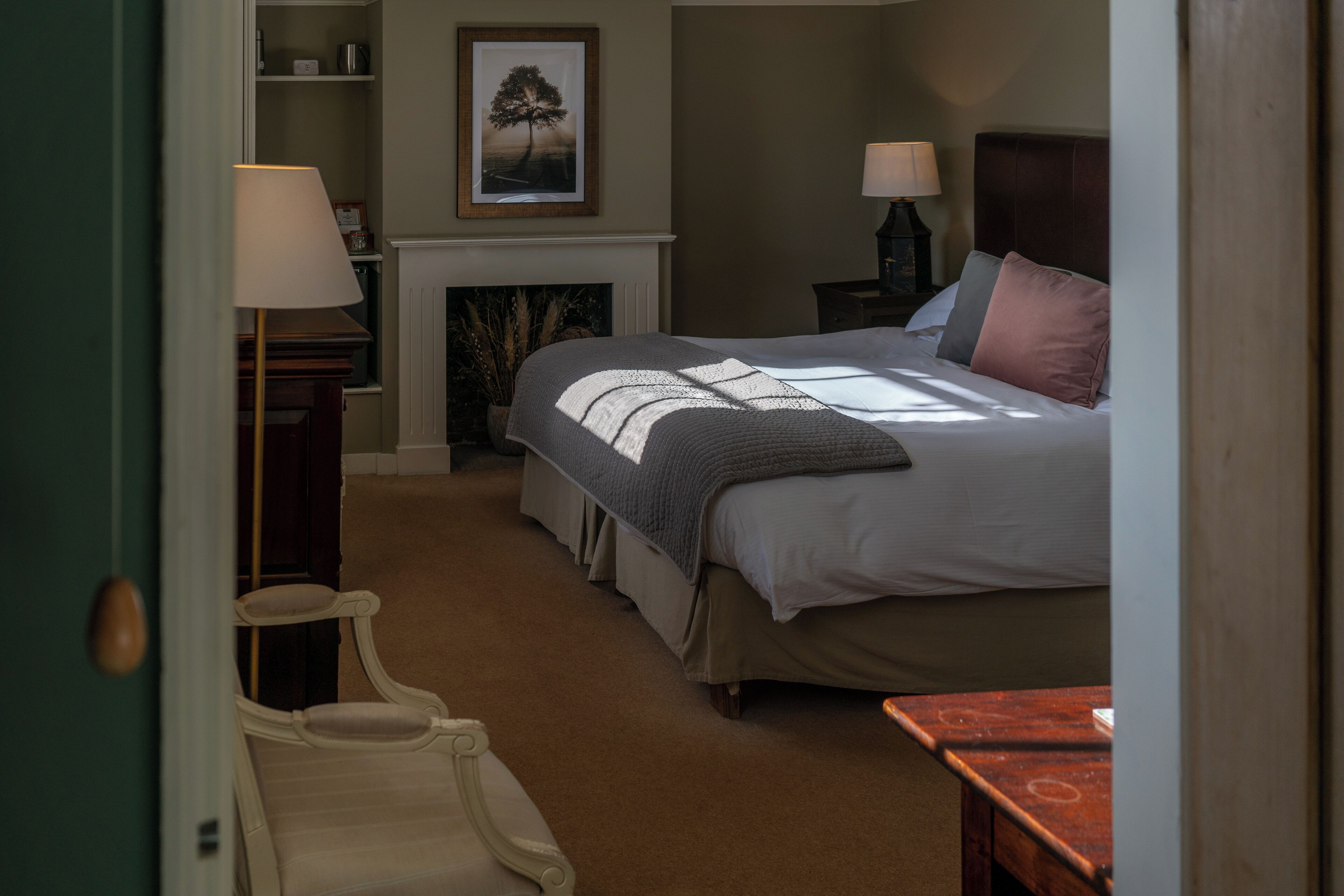 A bedroom with a bed, bedside tables, a chair, a fireplace, and a framed picture on the wall.