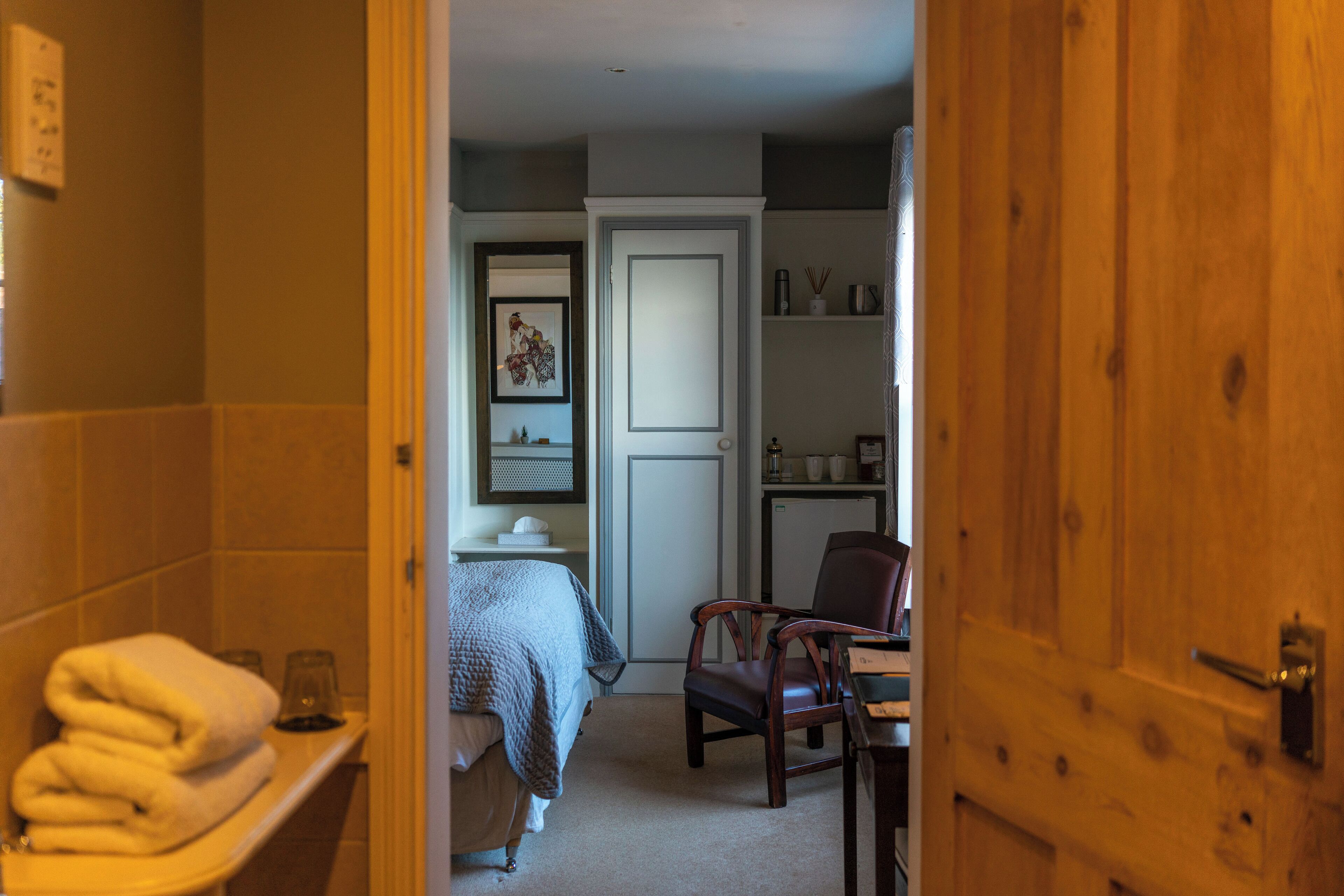 Hotellihuone, jossa on sänky, tuoli, työpöytä ja ovi, joka johtaa toiseen huoneeseen.