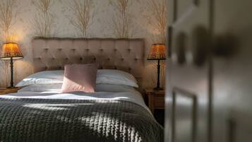 A neatly made bed with a tufted headboard, two bedside lamps, and a patterned wallpaper.