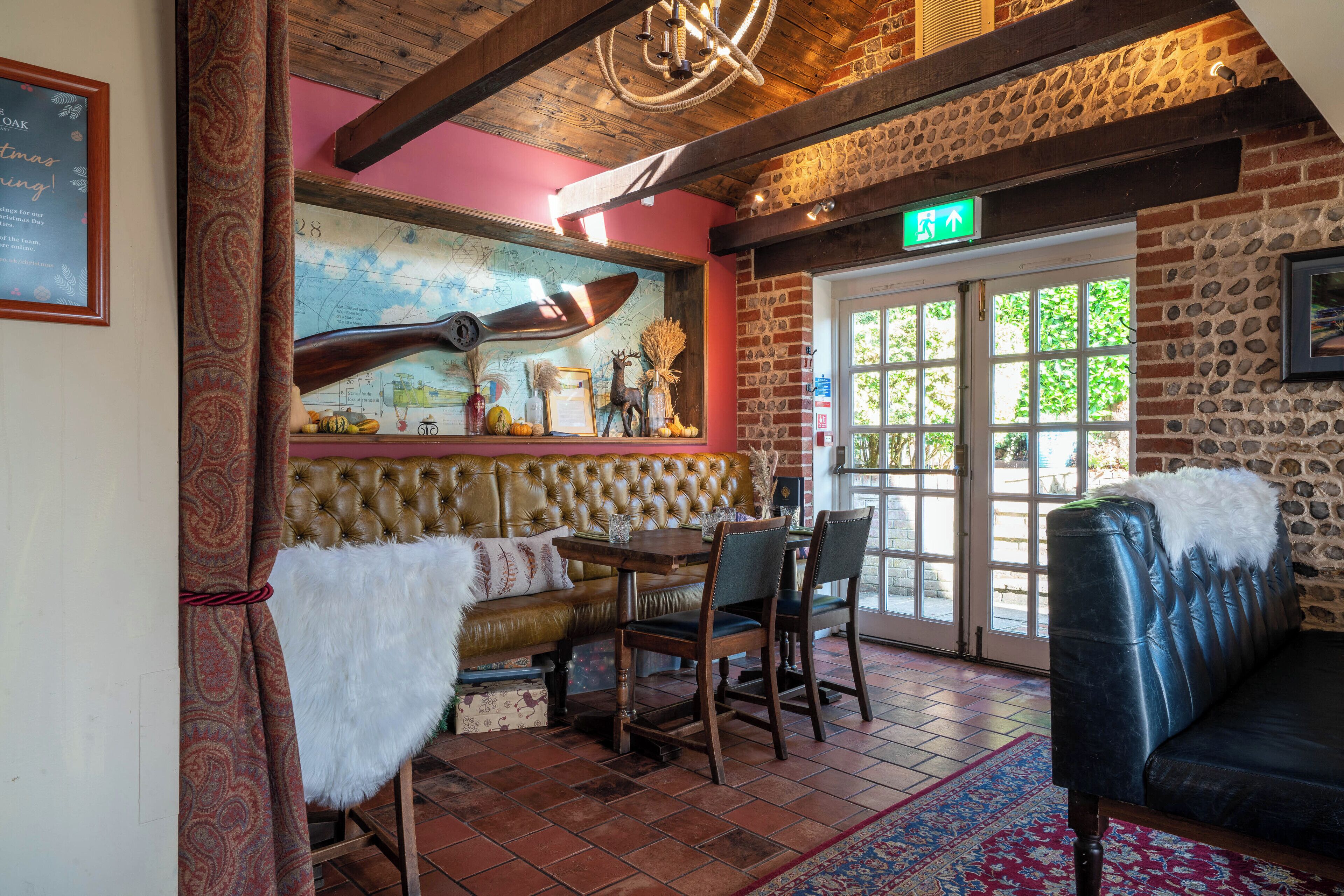 Un intérieur chaleureux avec un plafond en bois, une carte accrochée au mur, un canapé en cuir, une table à manger avec des chaises et un mur en pierre.