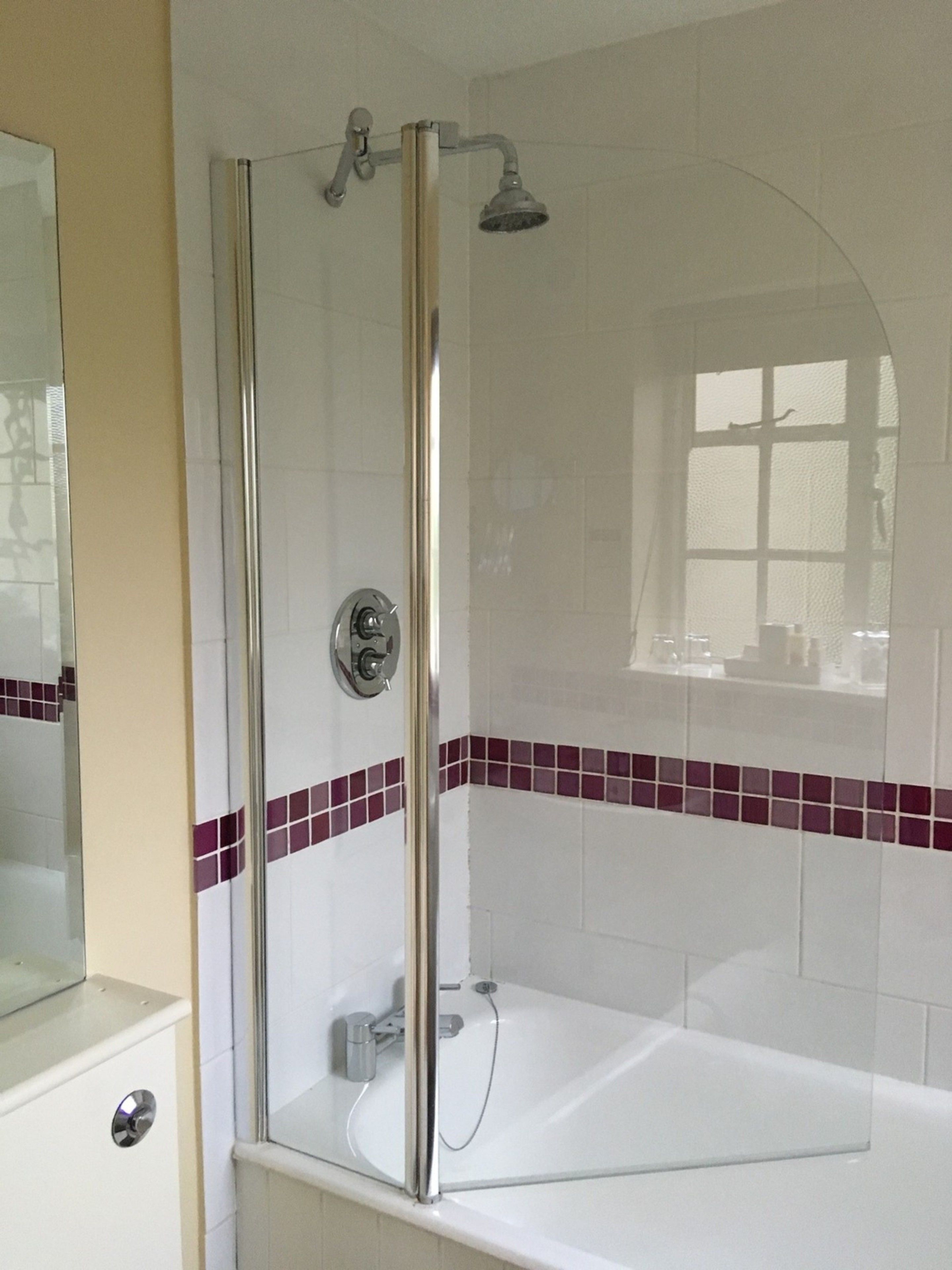 Ducha envuelta en vidrio con cabezal de ducha manual, puerta de cristal y pared de azulejos con detalle rojo.
