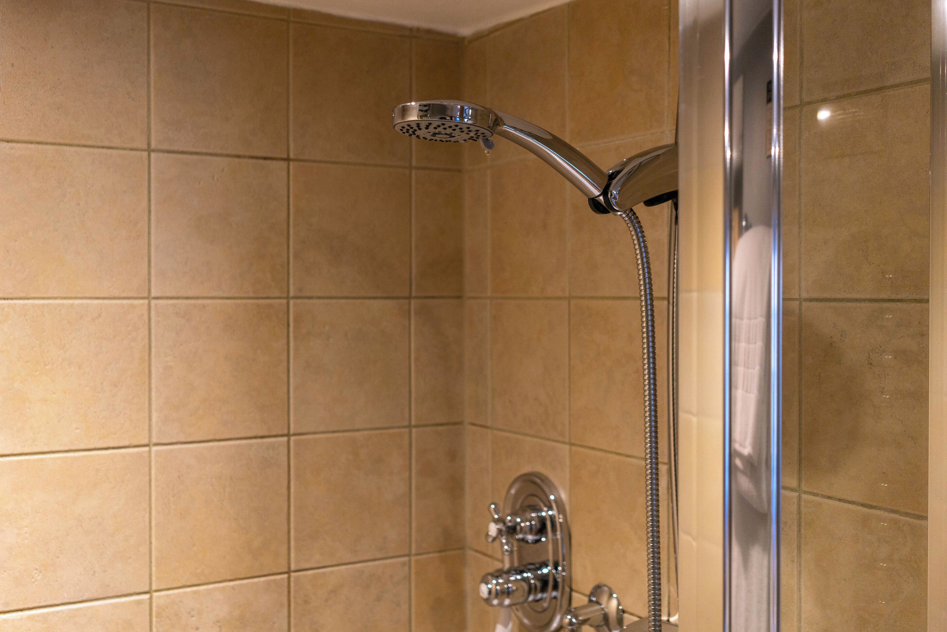 A bathroom with beige tiles, a chrome showerhead, and a visible shower hose.
