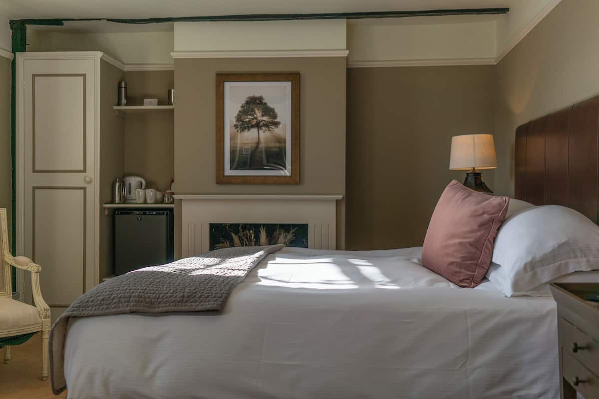 Quarto bem arrumado com cama, luminária de cabeceira e lareira com um quadro emoldurado acima.