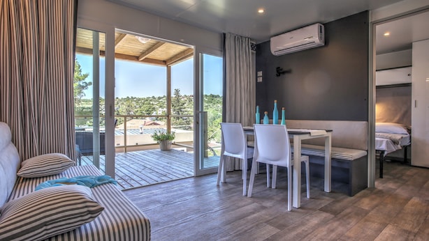 A modern room with a sofa, a dining table with chairs, a small bed, and a sliding glass door leading to an outdoor area. - Camp Rehut - Campsite (Murter-Kornati)