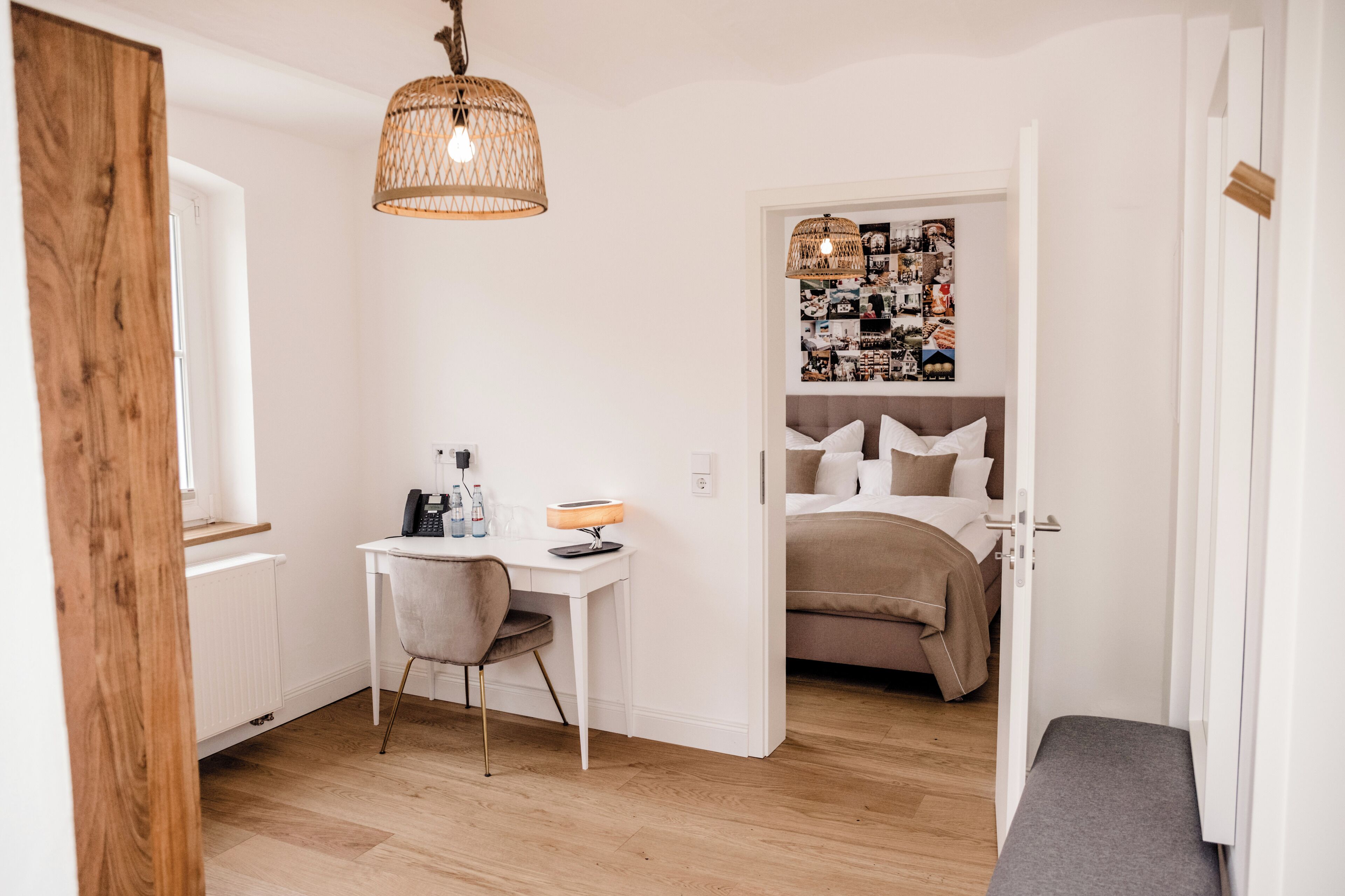 Habitación compacta con cama, escritorio y silla. Se observa una pared con un collage de fotos y una lámpara colgante.