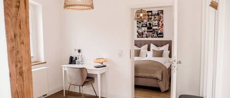 Habitación compacta con cama, escritorio y silla. Se observa una pared con un collage de fotos y una lámpara colgante.