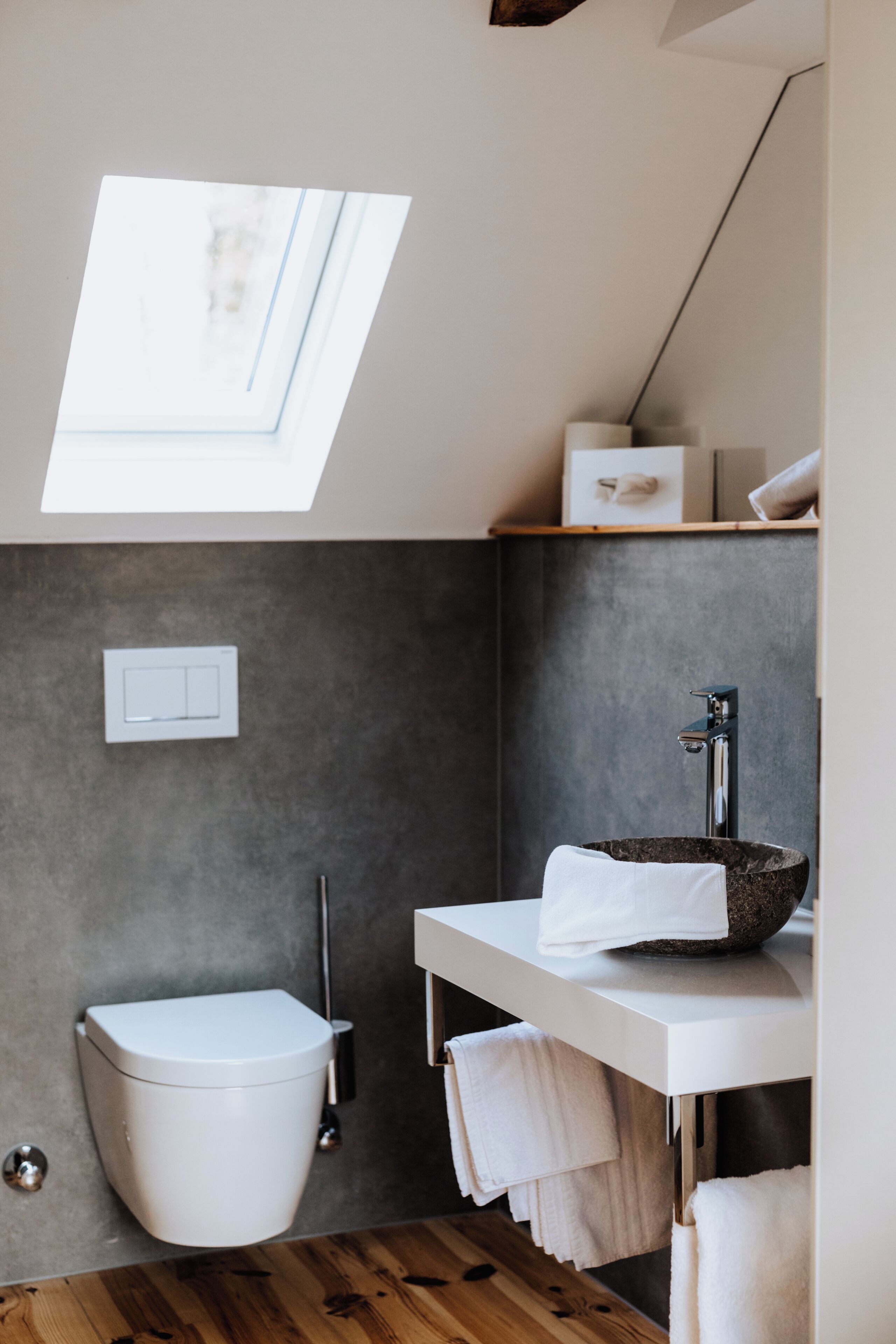 Un baño moderno con tragaluz, inodoro blanco, lavabo empotrado con lavamanos de piedra y suelo de madera.