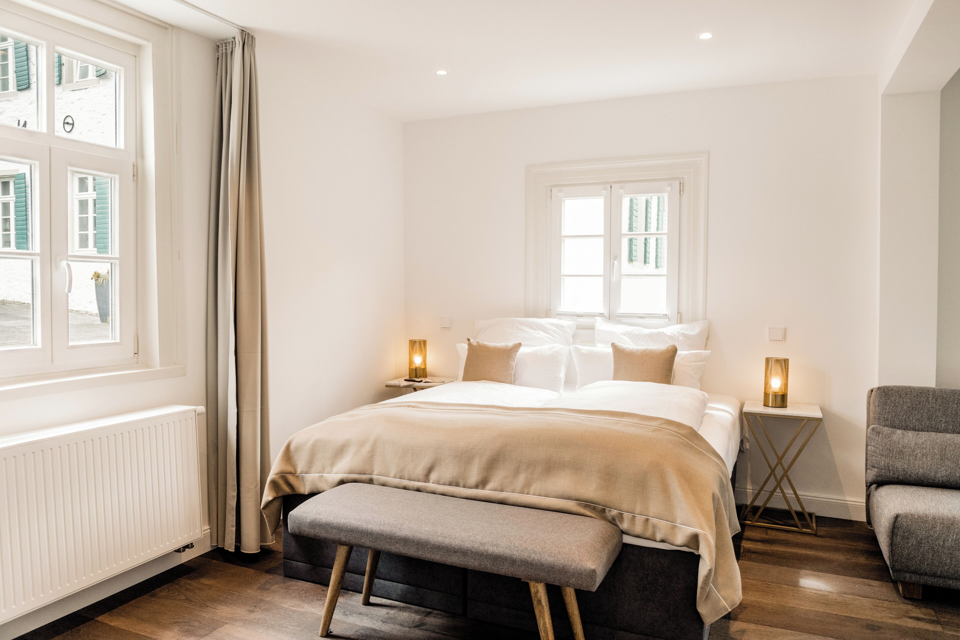 Un dormitorio con cama, mesitas de noche, un banco y una ventana con cortinas.