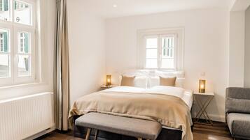 Un dormitorio con cama, mesitas de noche, un banco y una ventana con cortinas.