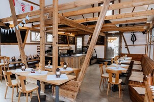 Um interior rústico de madeira com tetos altos, vigas aparentes e uma longa mesa de jantar comunitária com bancos.