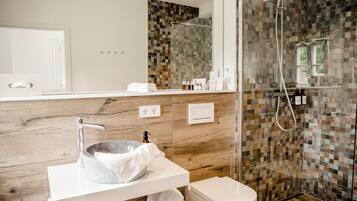 A modern bathroom with a stone sink, white fixtures, and a mosaic shower wall.